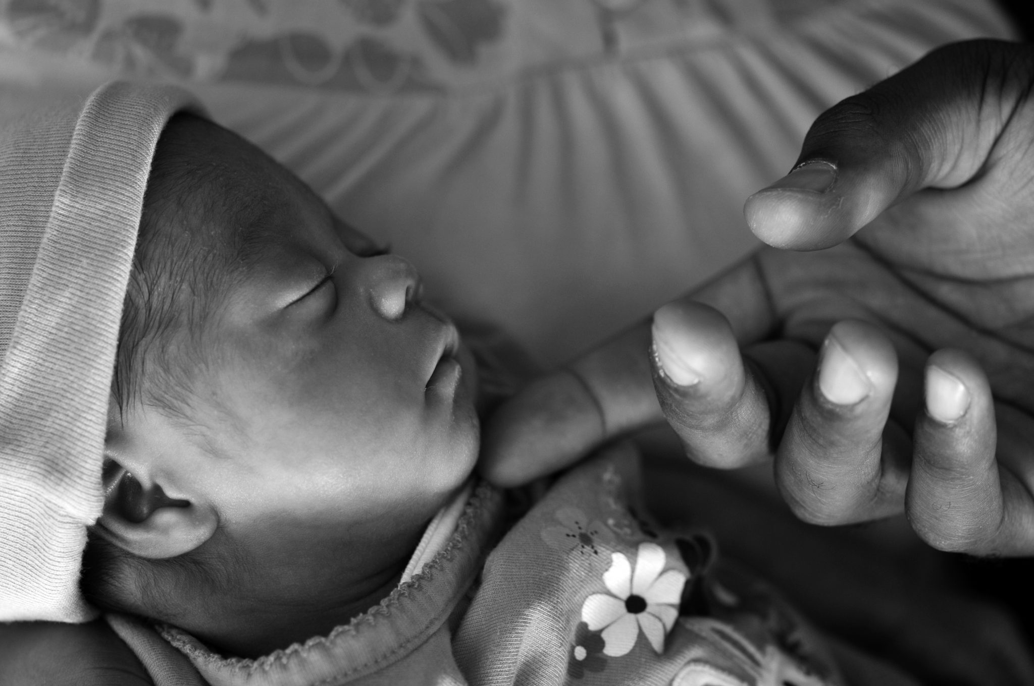 An adult hand gently touching a newborn's face