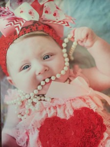 Baby girl dressed in a very frilly headband and dress playing with a string of pearls