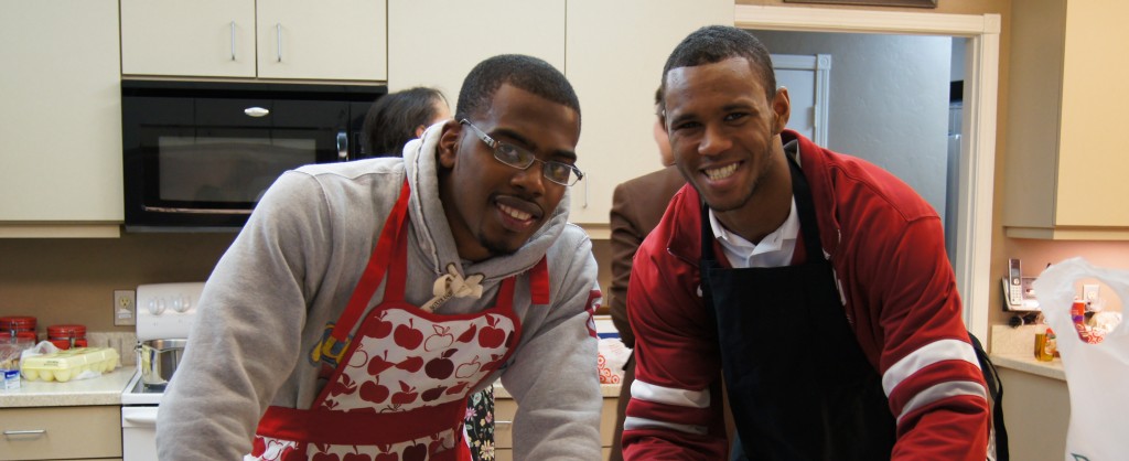 Two young men with aprons inside a kitchen smiling at the camera