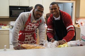 Two young men with aprons inside a kitchen smiling at the camera
